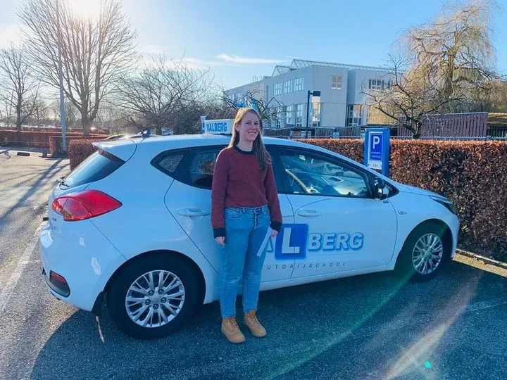 Geslaagde leerling poseert trots bij de lesauto